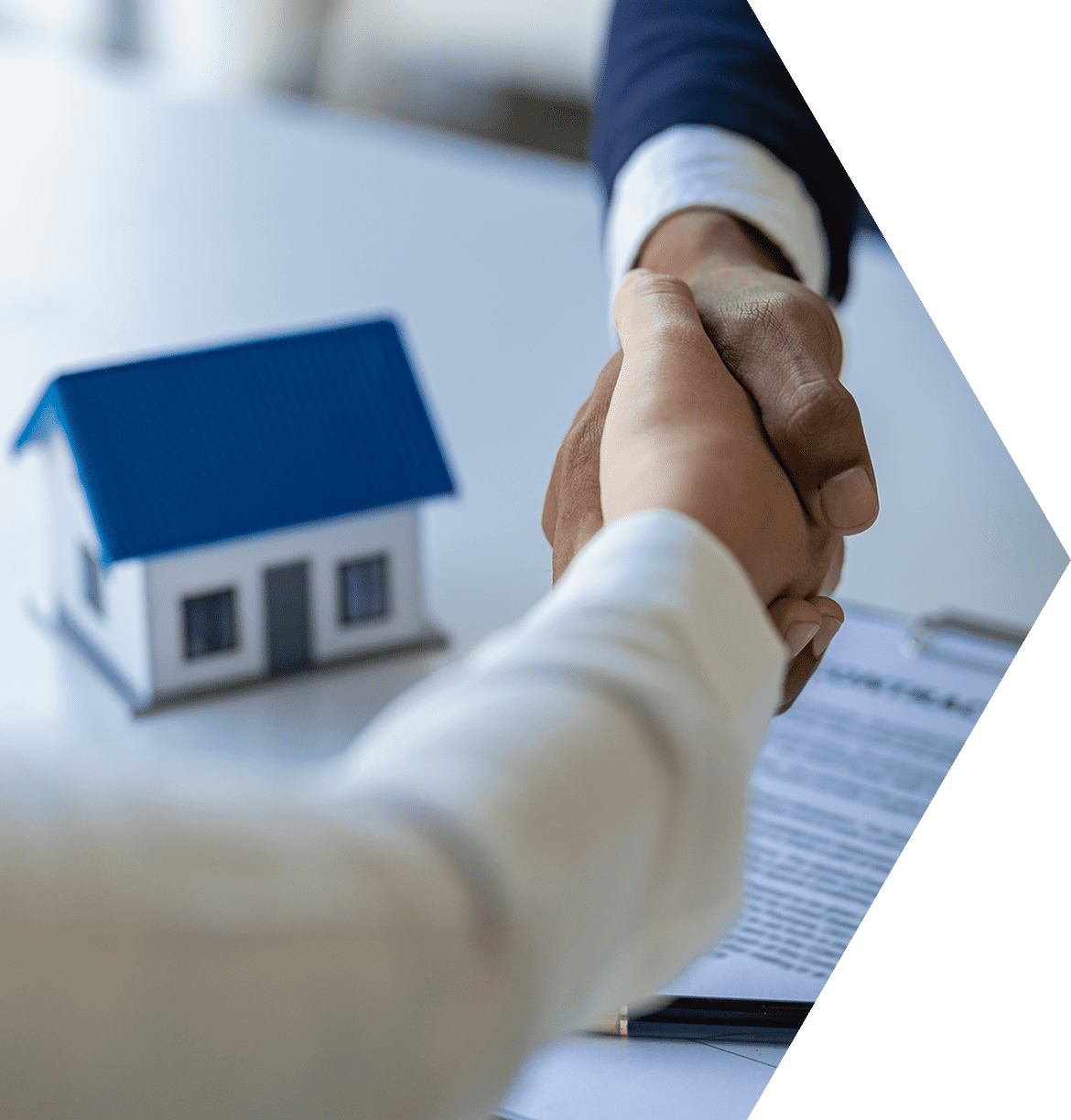 Two people shaking hands over a table with paperwork.